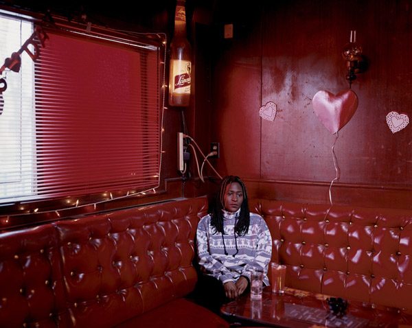 woman sits alone in red corner booth