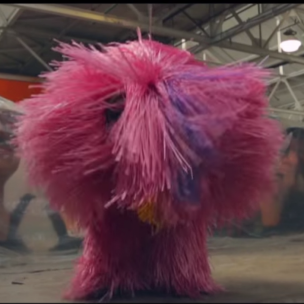 pink fabric figure stands in front of large ceramic heads