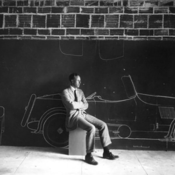 black and white photo of man posing next to sketch of car (zoom)