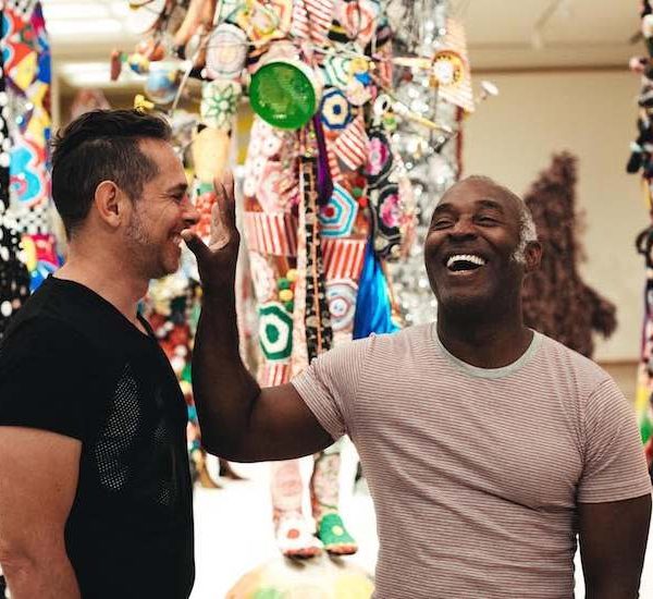 Two men in t-shirts smiling next to fabric sculptures