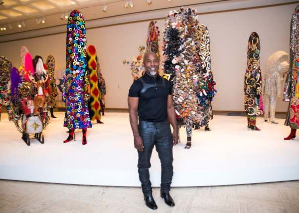 Nick Cave poses next to collection of sculptures with bright fabrics