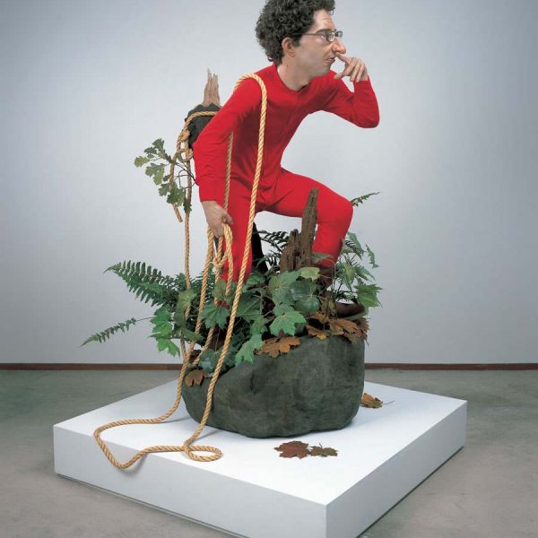 sculpture of man in red standing in plants