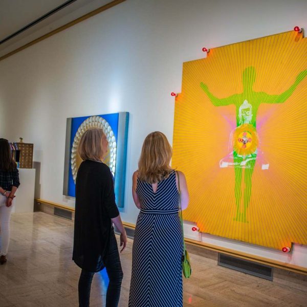 two women observe large neon painting of human figure with Buddha