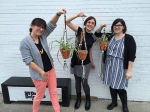 three women hold hanging plants