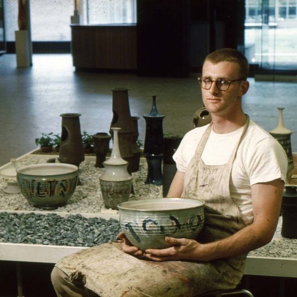 John Glick sitting at table with ceramics display