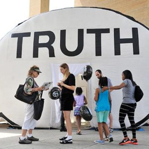 assortment of figures stand outside truth booth inflatable speech bubble