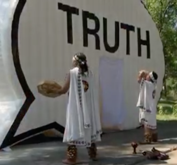 news screenshot of two people standing outside of truth booth inflatable speech bubble