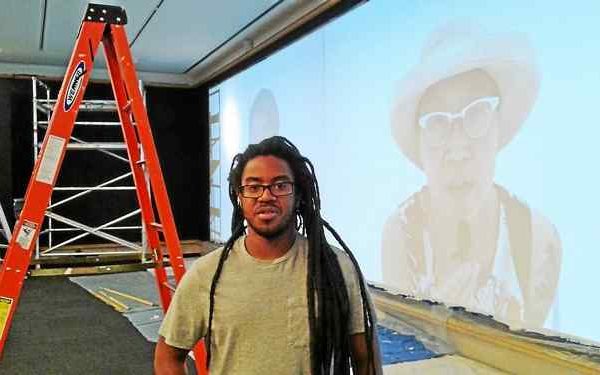 man with dreadlocks stands in front of projector screen