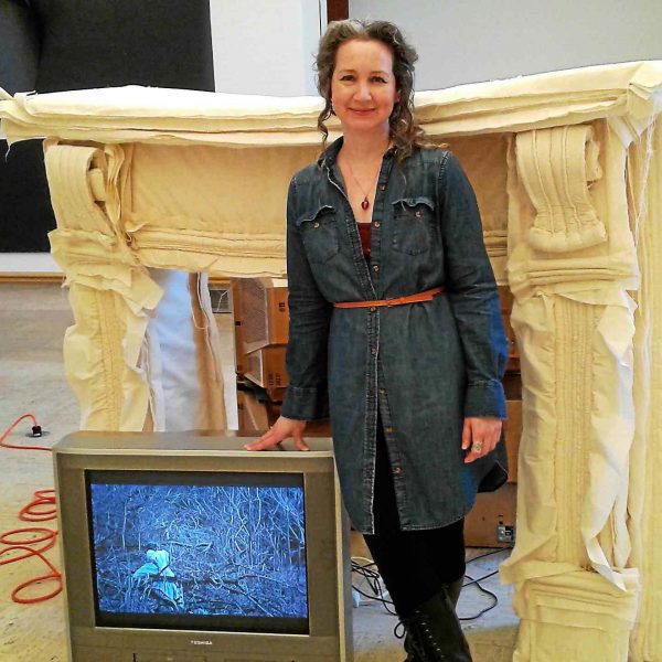 woman smiles next to art piece with television