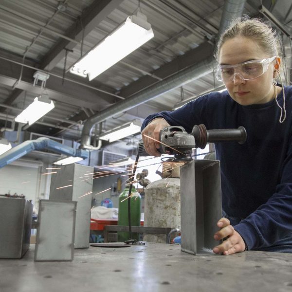 woman with safety goggles carves metal box