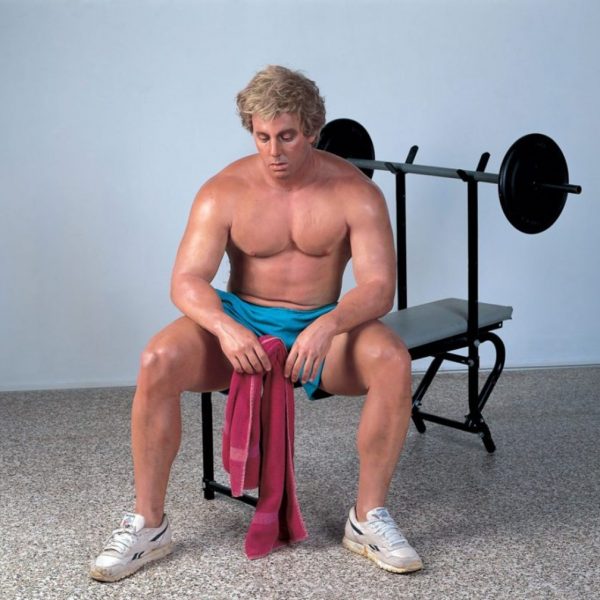 man sitting on exercise bench with maroon towel and blue shorts
