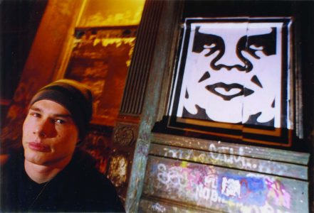 Man in hat stands next to Obey sign