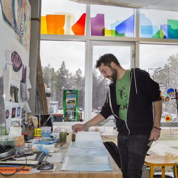 man in black hoodie stands at table as he paints