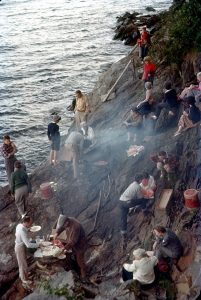 People sit and eat on cliffside next to water