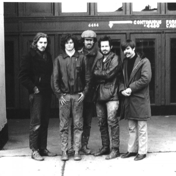 Five men in dark jackets stand in front of a doorway